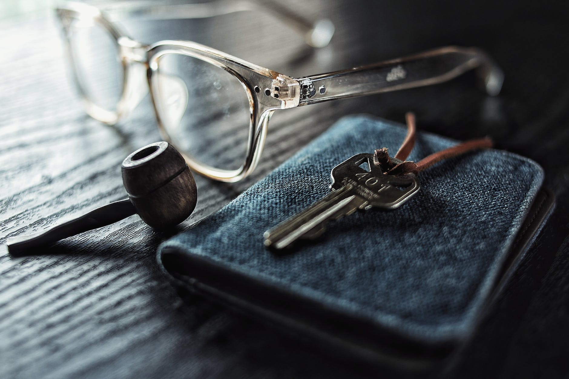 selective focus photo of silver key beside brown smoking pipe and clear eyeglasses